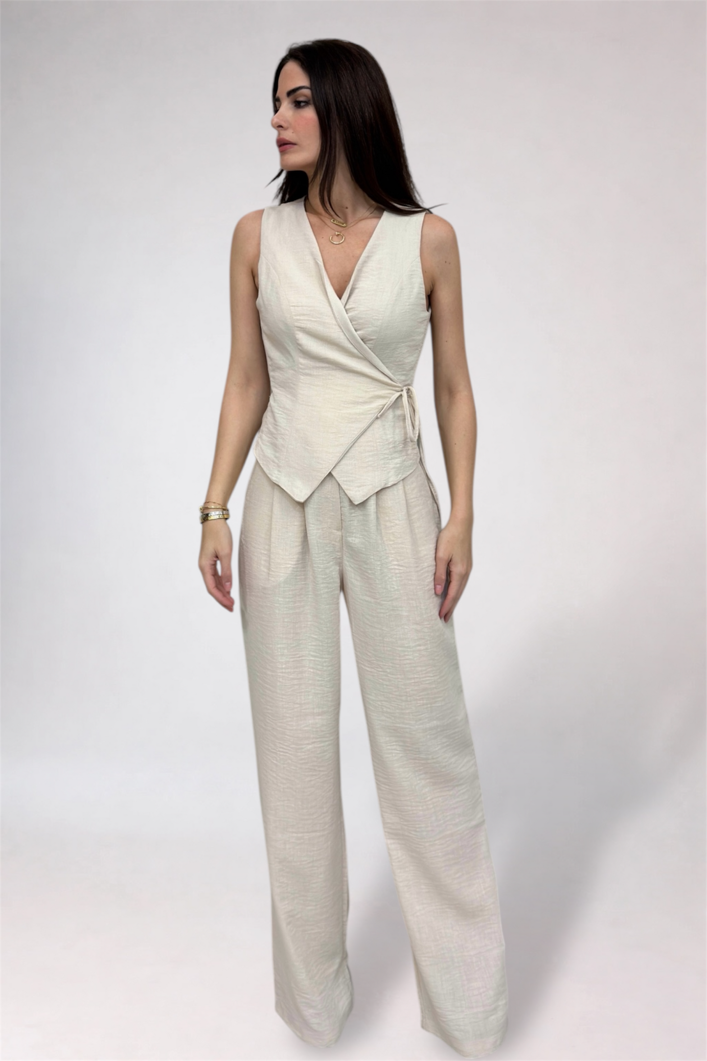 Woman wearing a light-colored sleeveless top and wide-leg pants on a white background