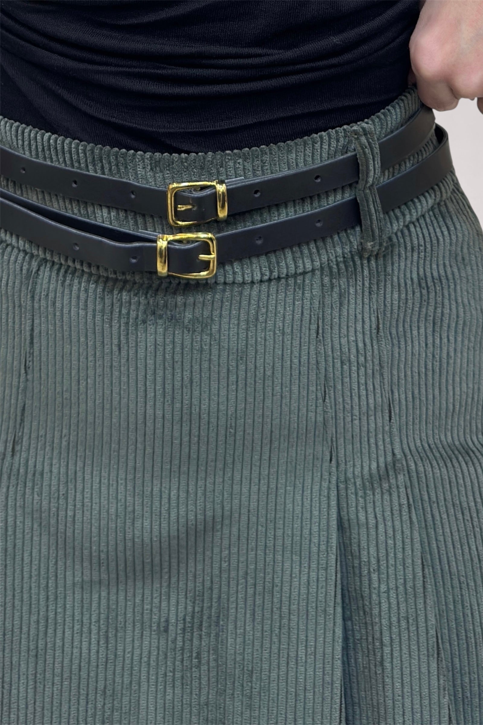 Person wearing a black belt with gold buckles and gray corduroy pants.