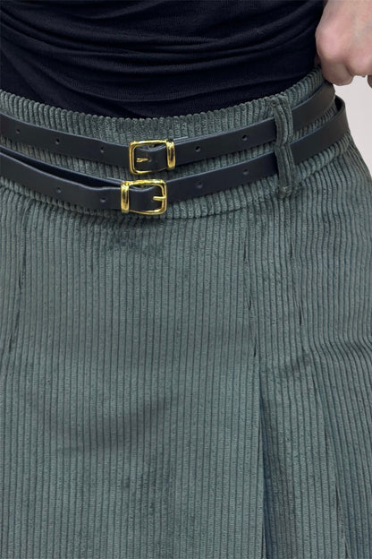 Person wearing a black belt with gold buckles and gray corduroy pants.