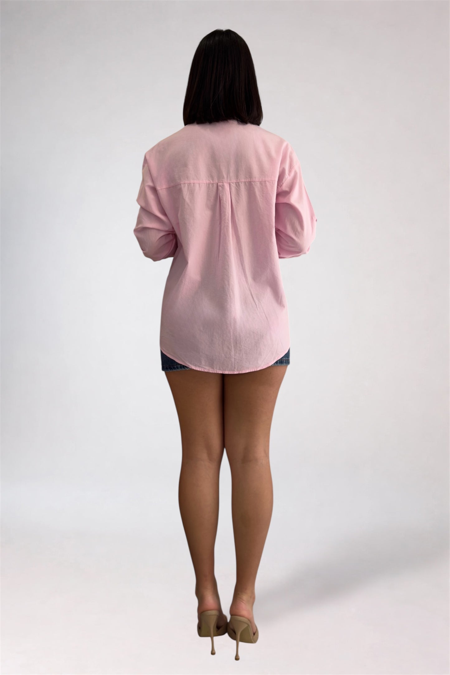 Person wearing a light pink shirt and denim shorts on a white background