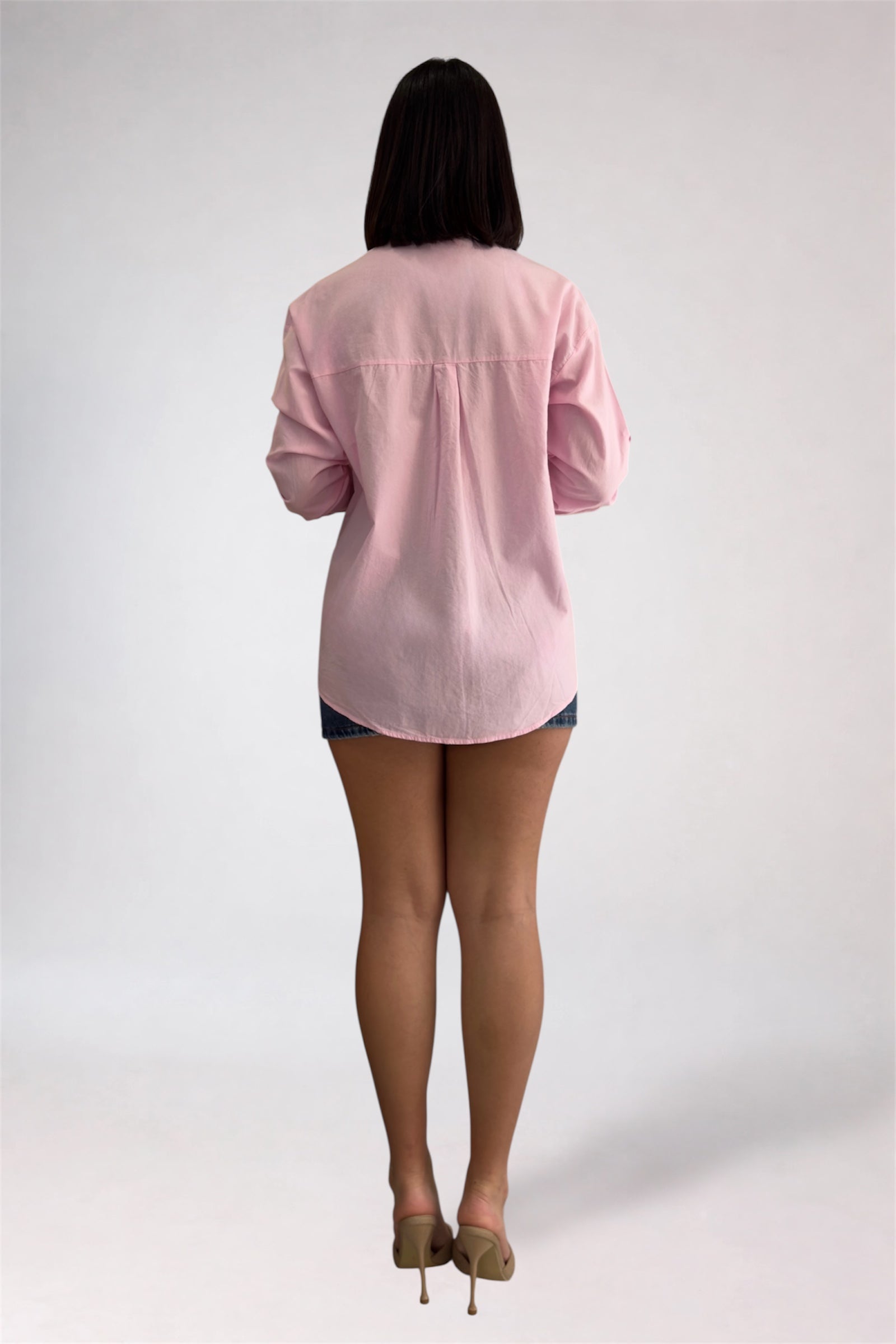 Person wearing a light pink shirt and denim shorts on a white background