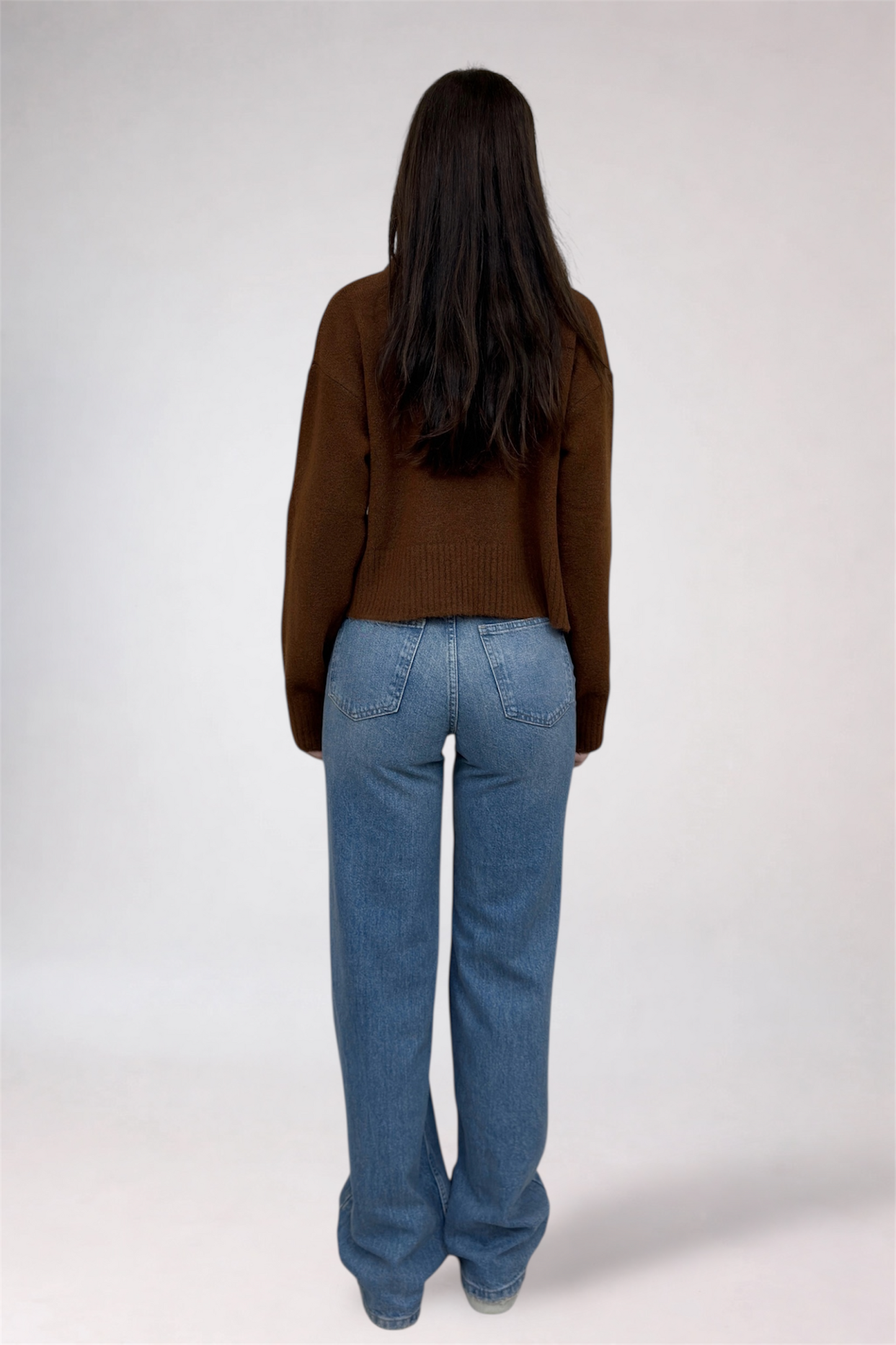 Person wearing a brown sweater and blue jeans on a white background