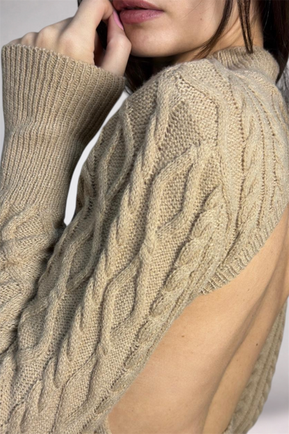 Close-up of a person wearing a beige cable knit sweater with a blurred background