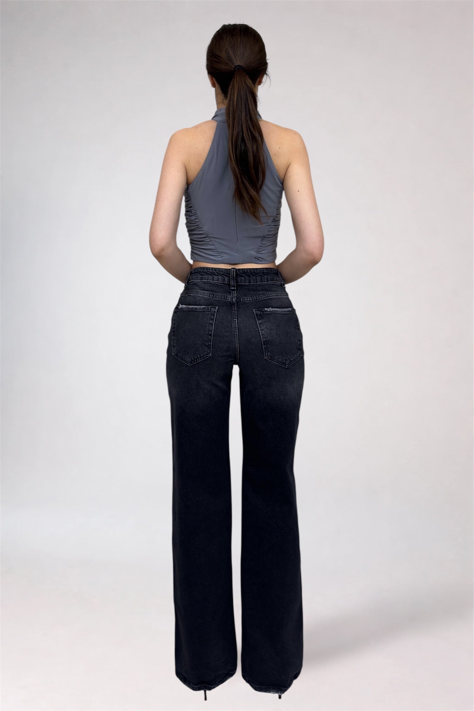 Person wearing black high-waisted jeans and a gray sleeveless top on a plain background