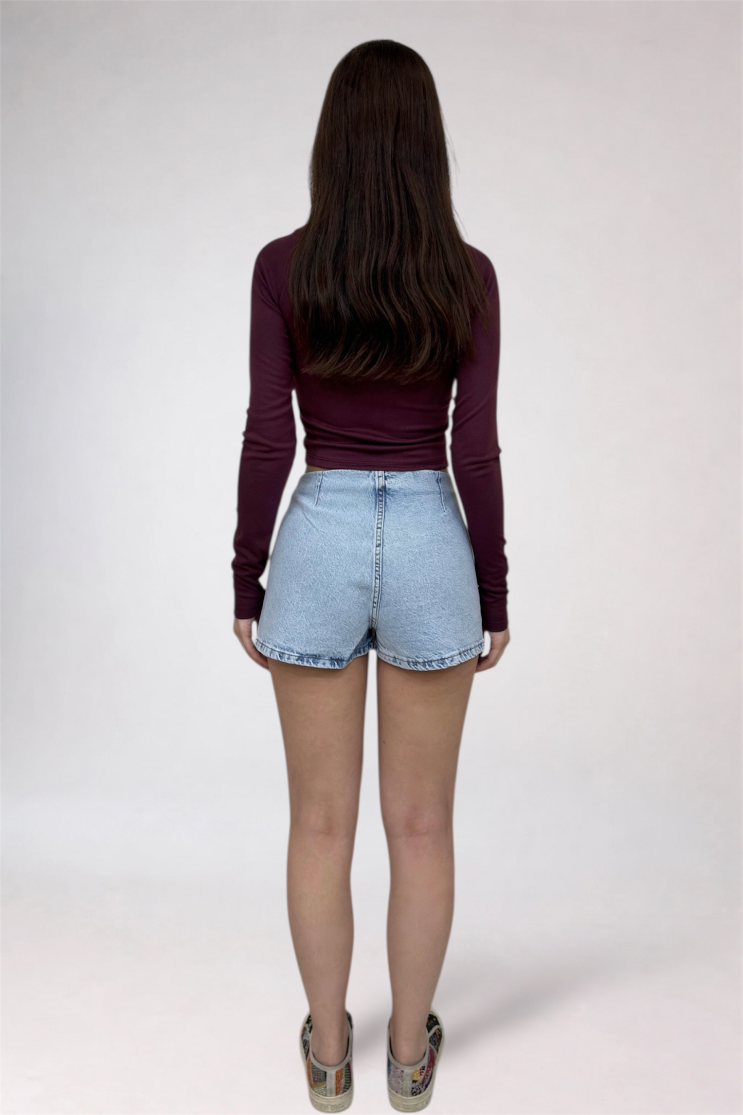 Person wearing a maroon long-sleeve top and light blue denim shorts on a white background