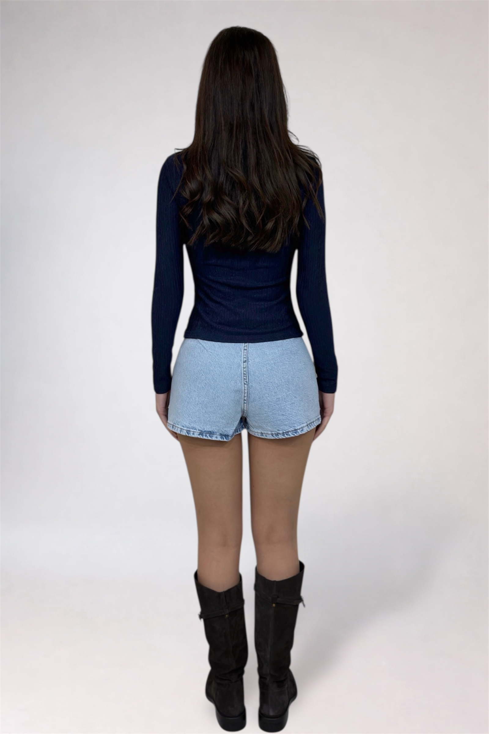 Person wearing a navy long-sleeve top and light blue denim shorts on a white background