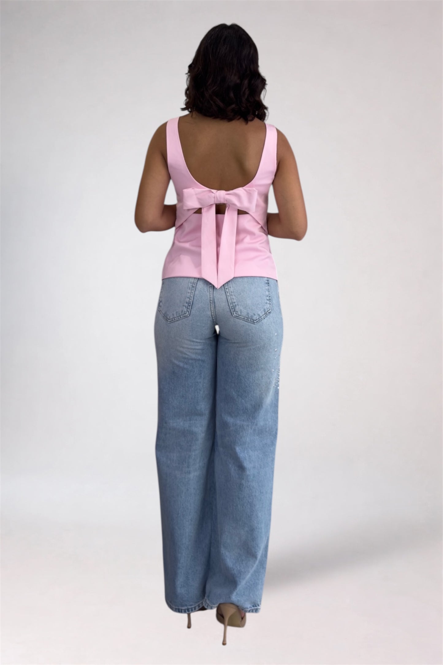 Woman wearing a pink sleeveless top and blue jeans on a white background
