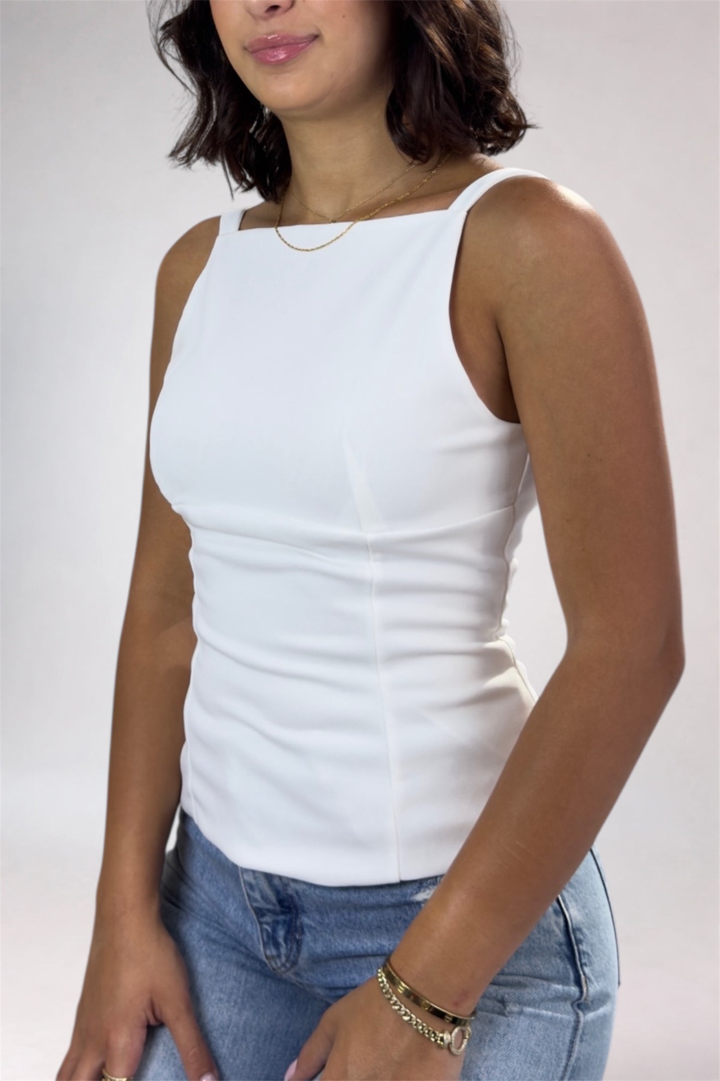 Woman wearing a white tank top and blue jeans on a plain background