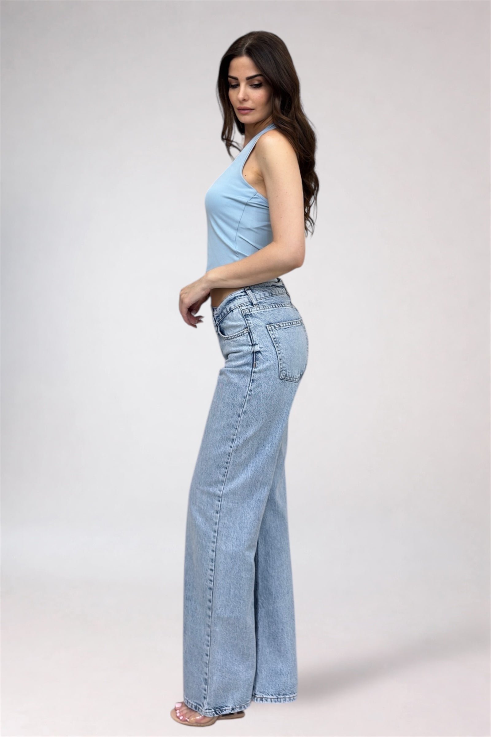 Woman wearing a light blue top and high-waisted jeans on a white background