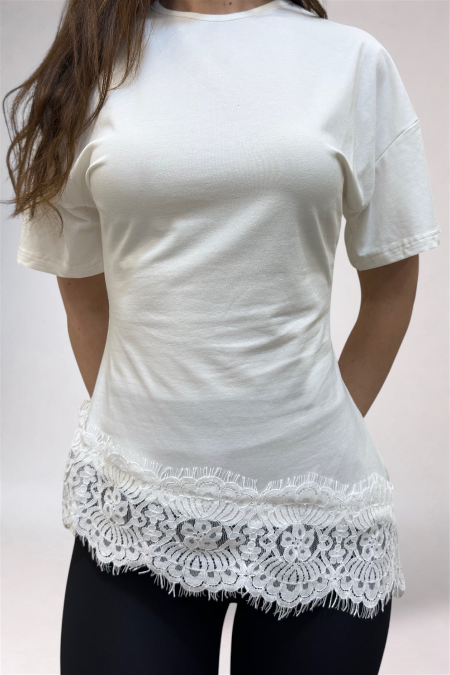 White t-shirt with lace trim worn by a person on a plain background