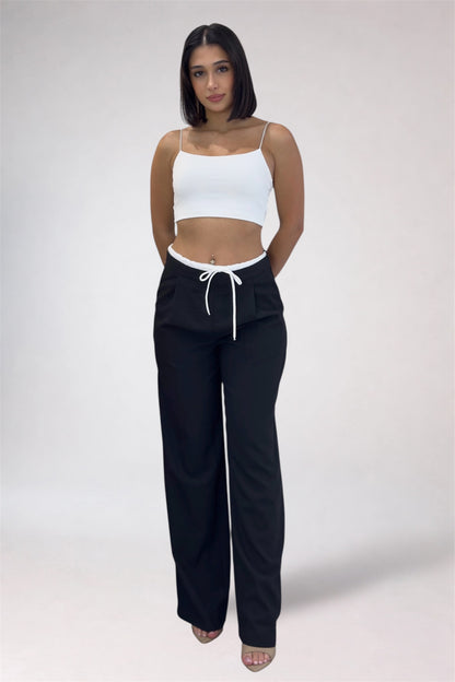 Woman wearing a white crop top and black pants with a drawstring on a plain background