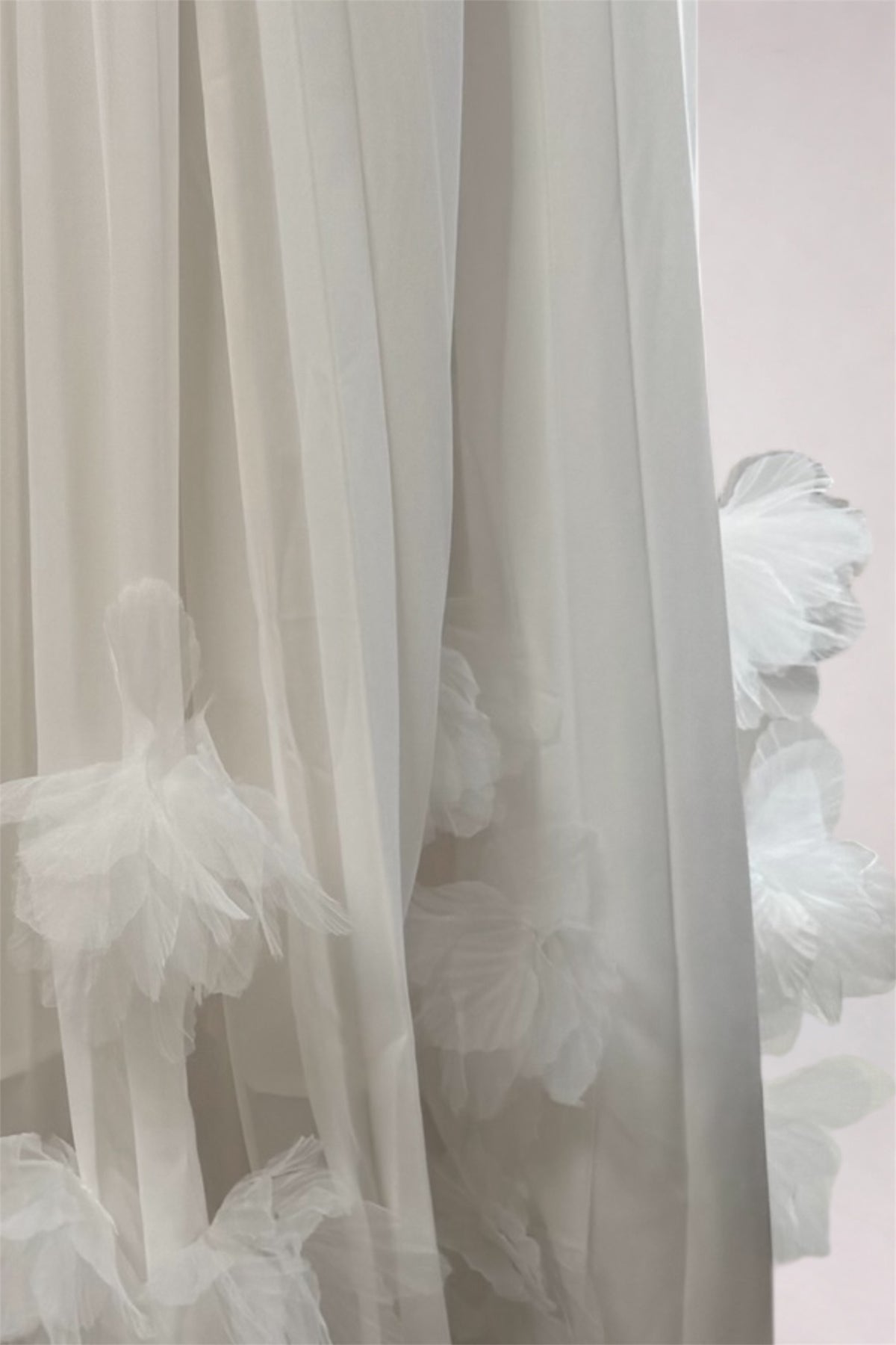 White sheer tulle curtains with layered ruffled fabric details, shown hanging against a pale pink wall.