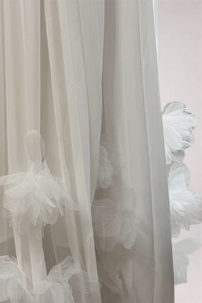 White sheer tulle curtains with layered ruffled fabric details, shown hanging against a pale pink wall.