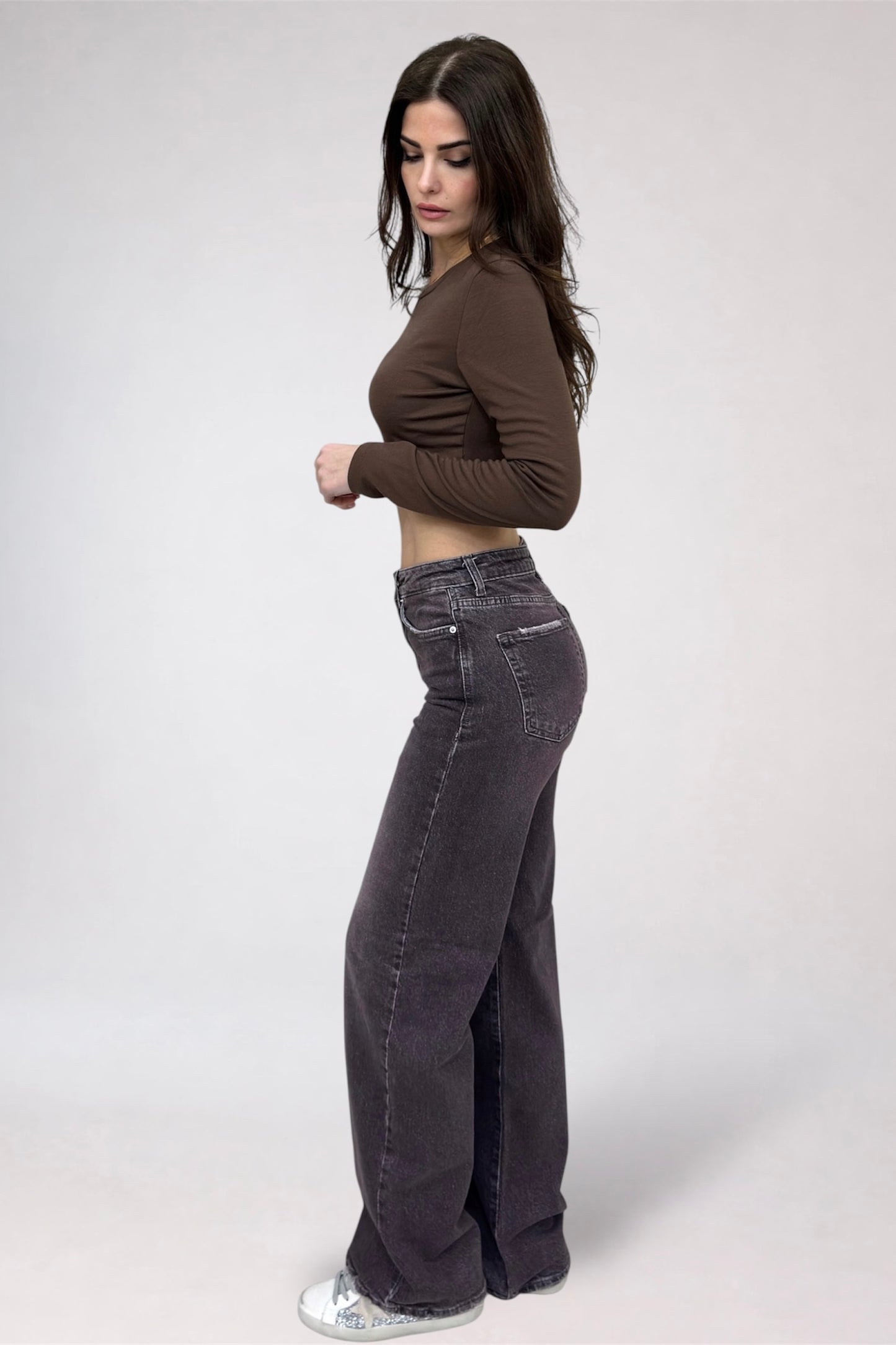 Woman wearing a brown long-sleeve top and dark jeans on a white background