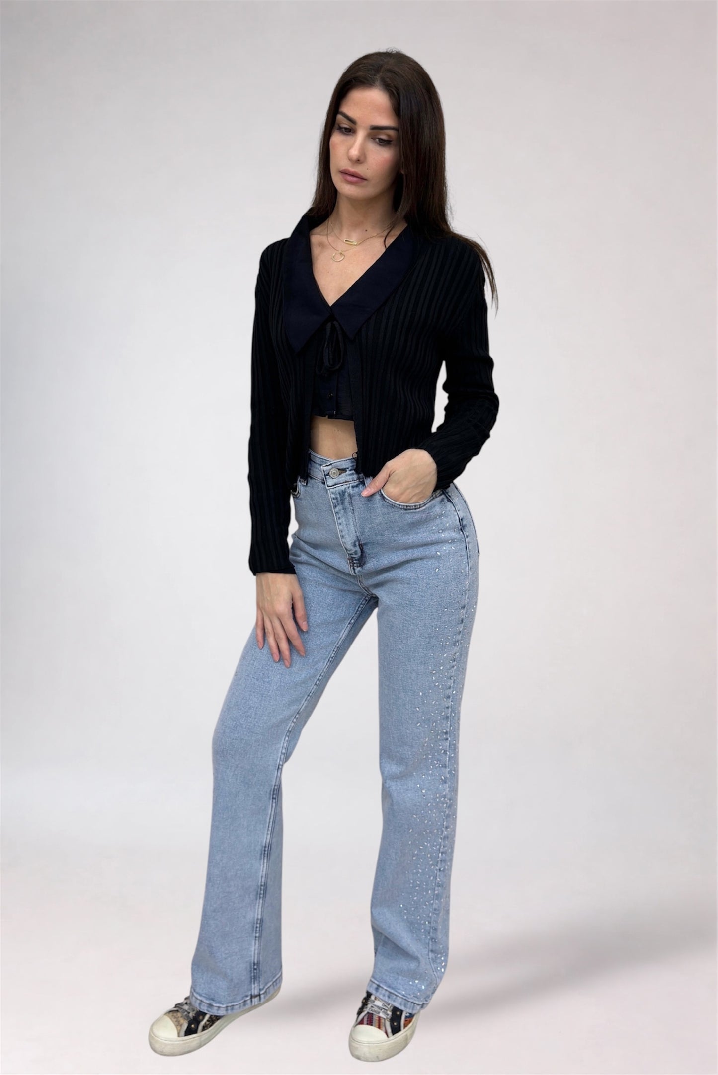 Woman wearing a black cardigan and light blue jeans on a white background
