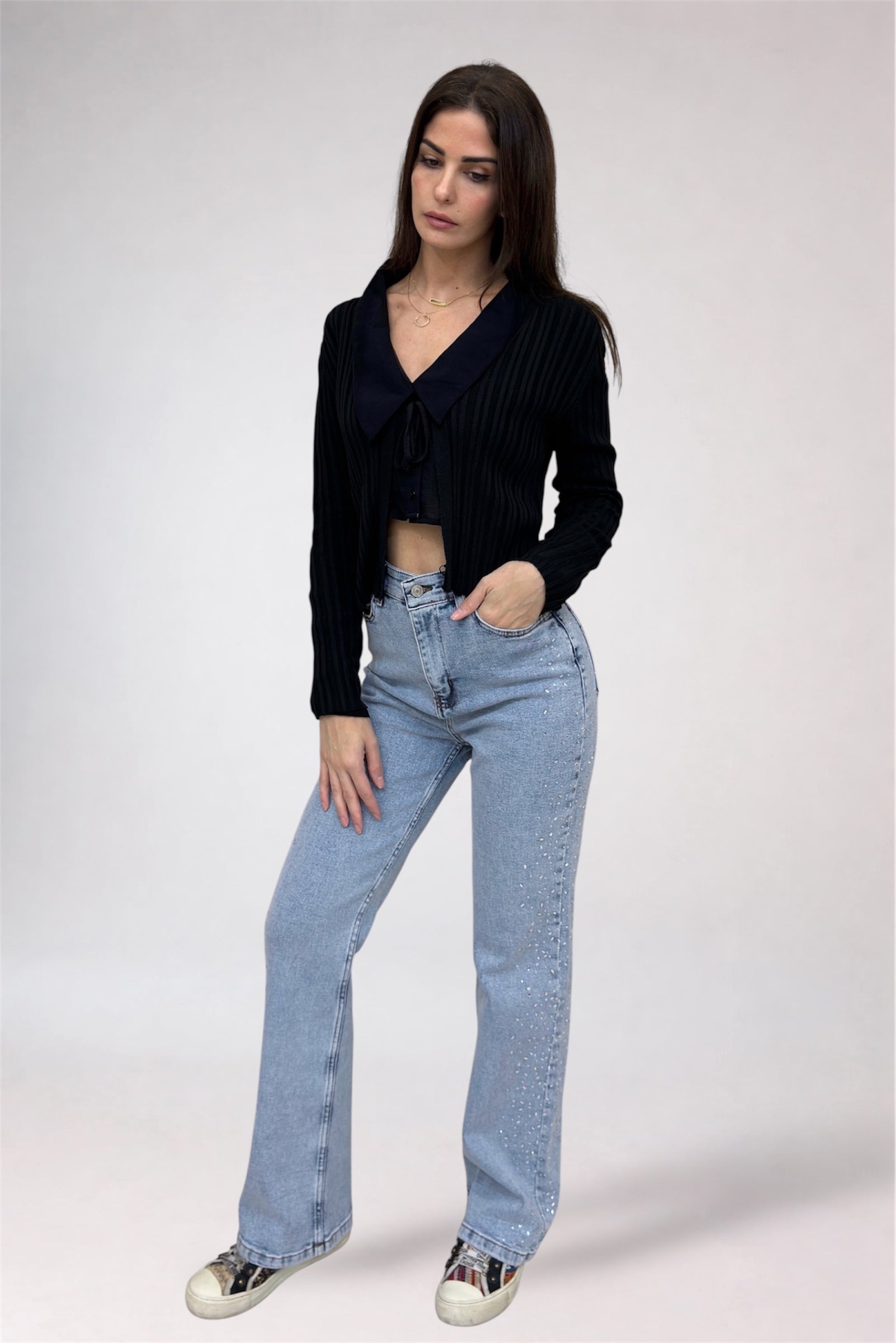 Woman wearing a black cardigan and light blue jeans on a white background