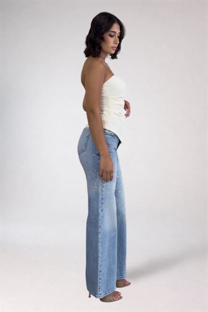 Woman wearing light blue flared jeans and a white top on a plain background