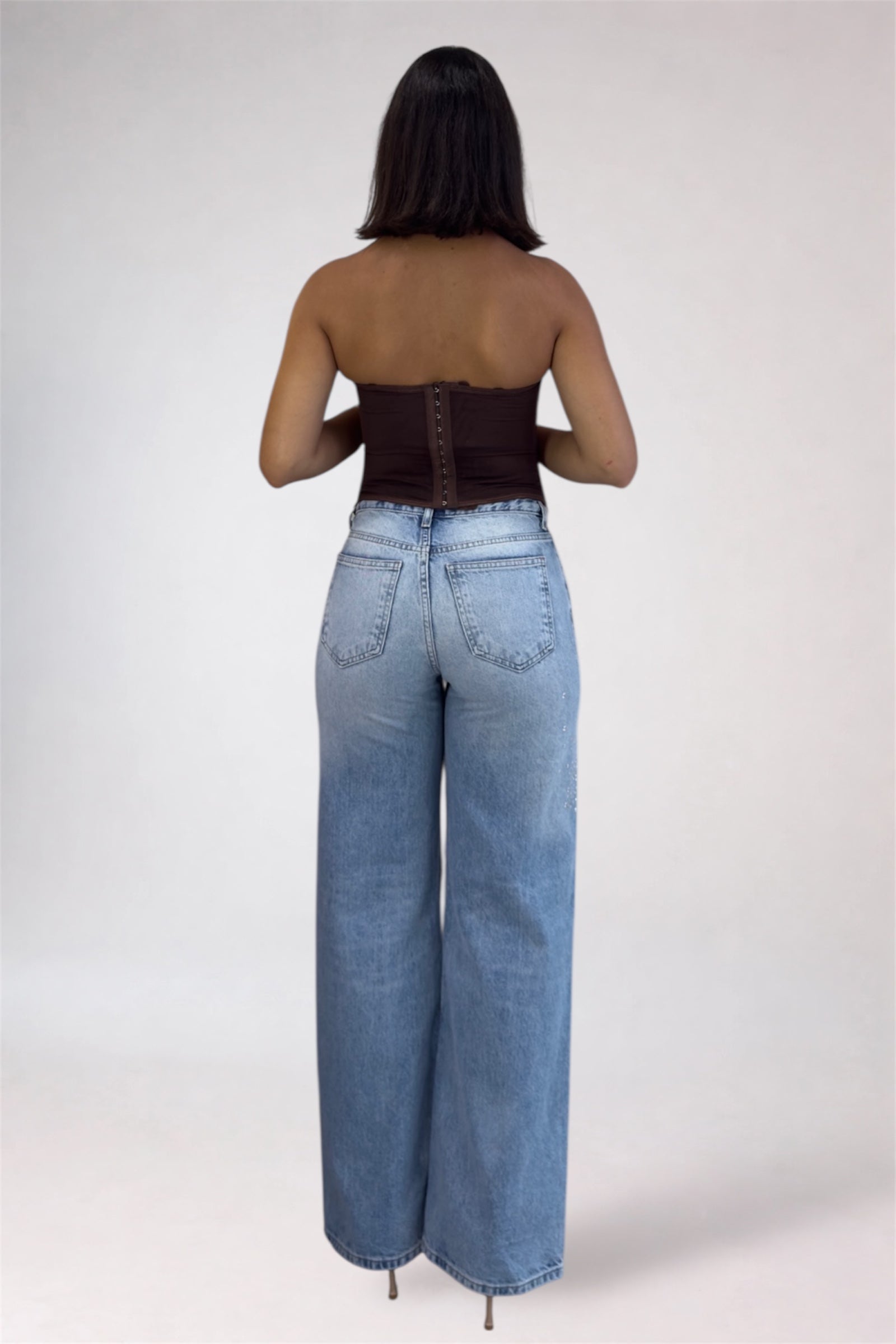 Person wearing high-waisted blue jeans and a strapless top on a white background