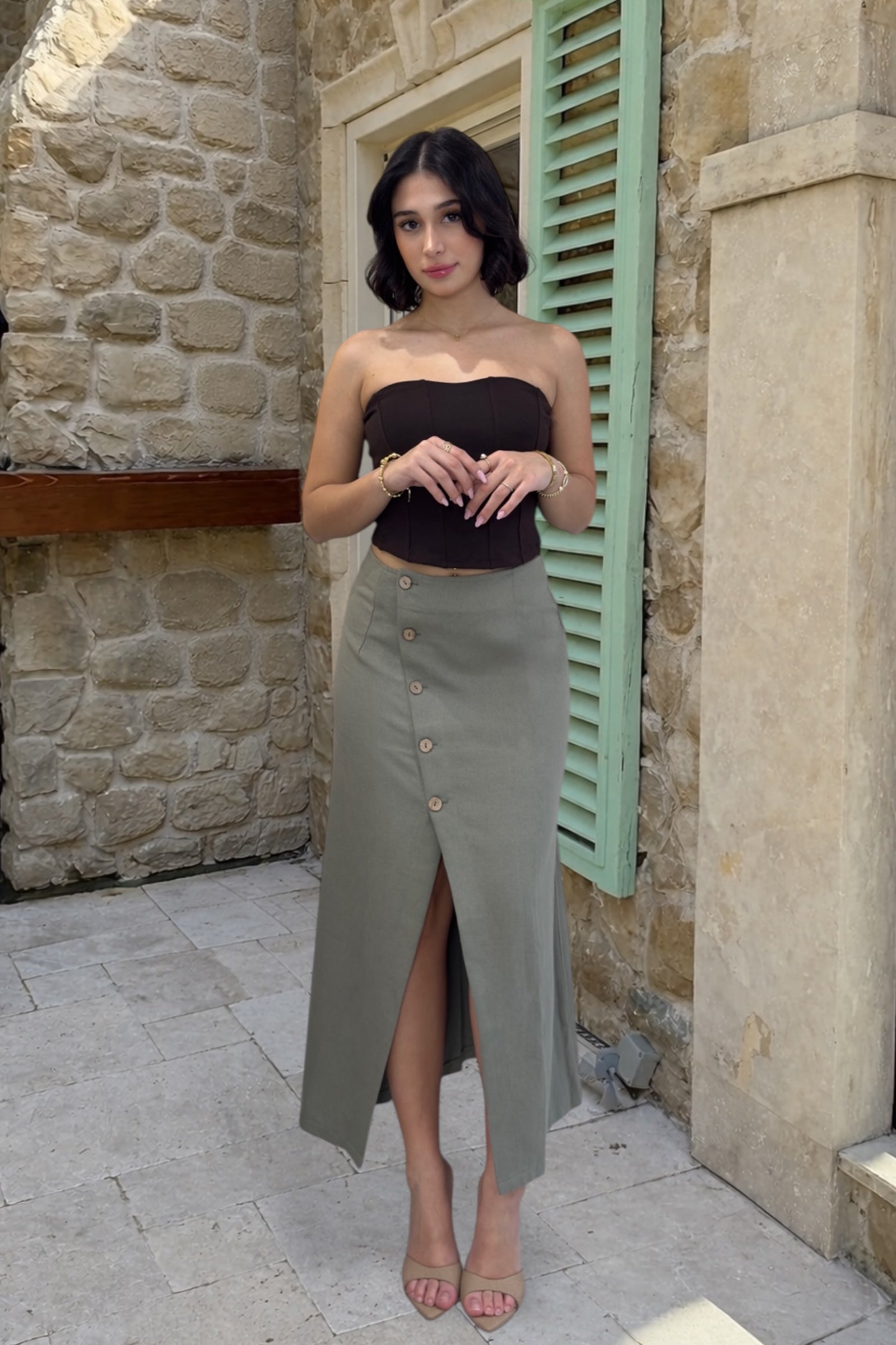 Woman wearing a black top and green skirt standing in front of a stone wall.