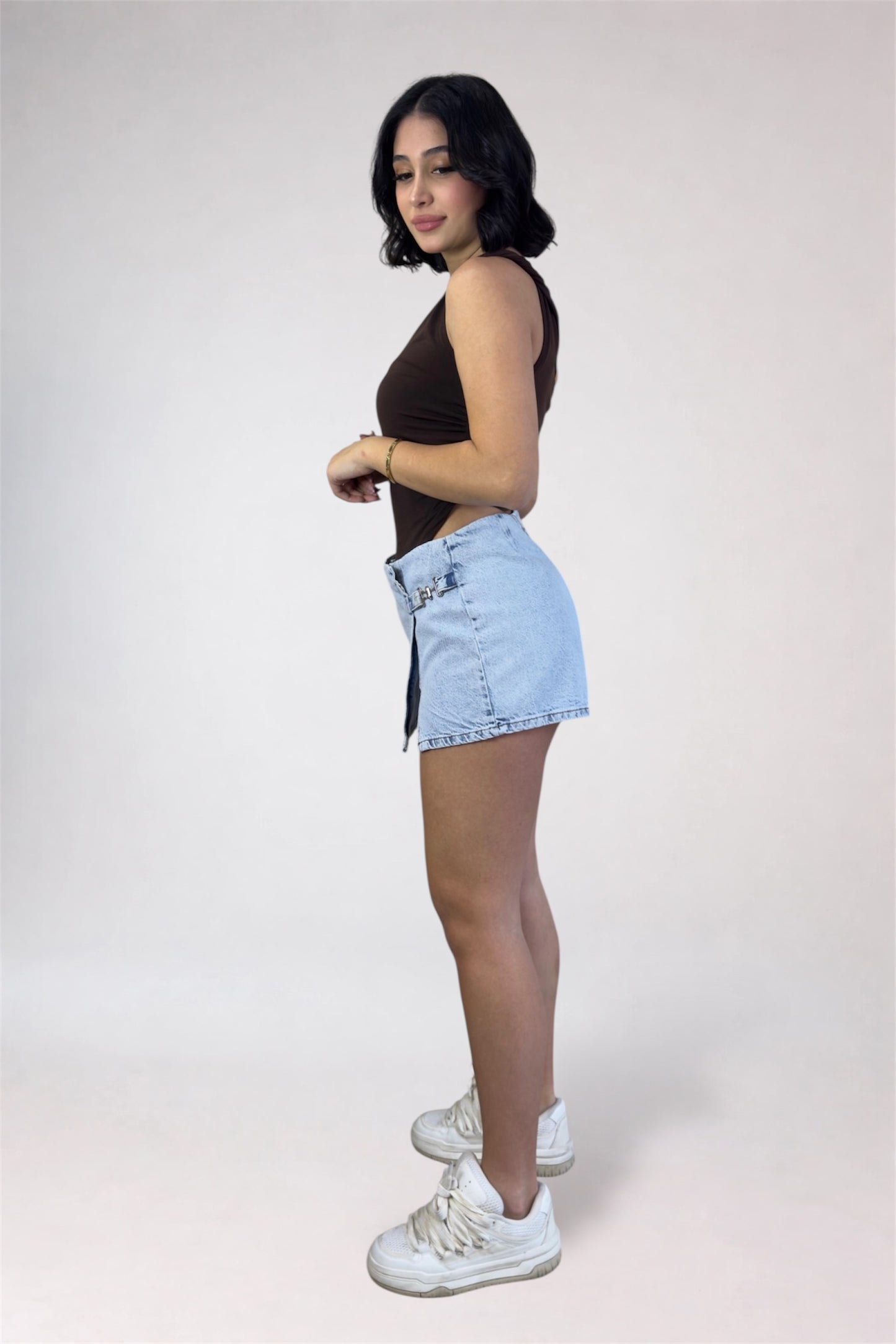 Woman wearing a black sleeveless top and light blue denim shorts on a white background