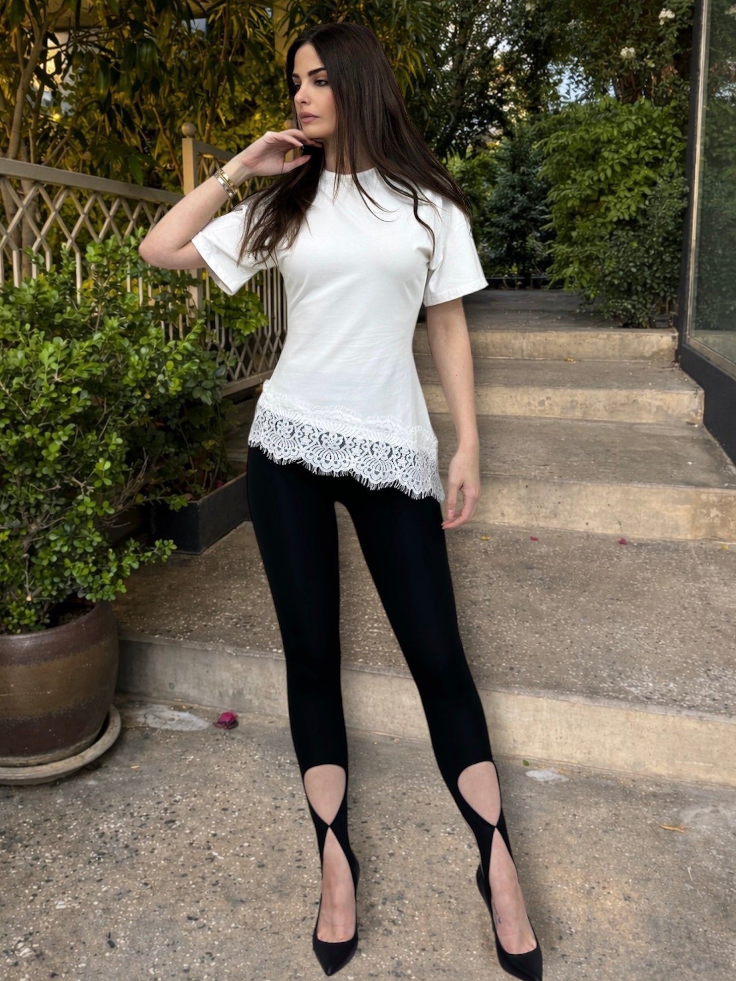Woman wearing a white top with lace details and black pants outdoors.