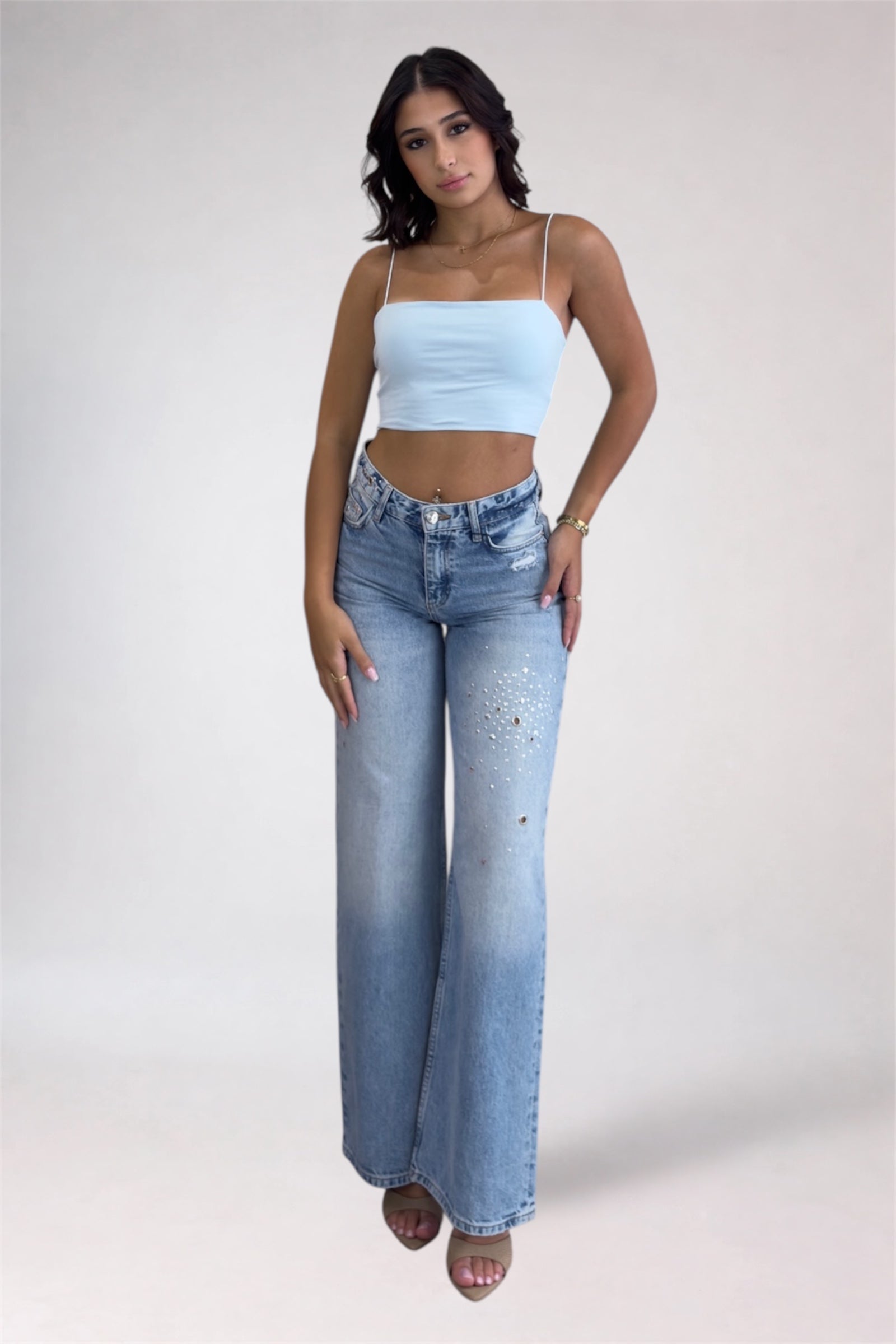 Woman wearing a light blue crop top and high-waisted jeans on a white background