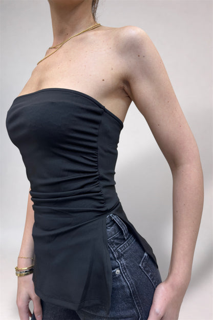 Person wearing a black strapless top and denim shorts on a plain background