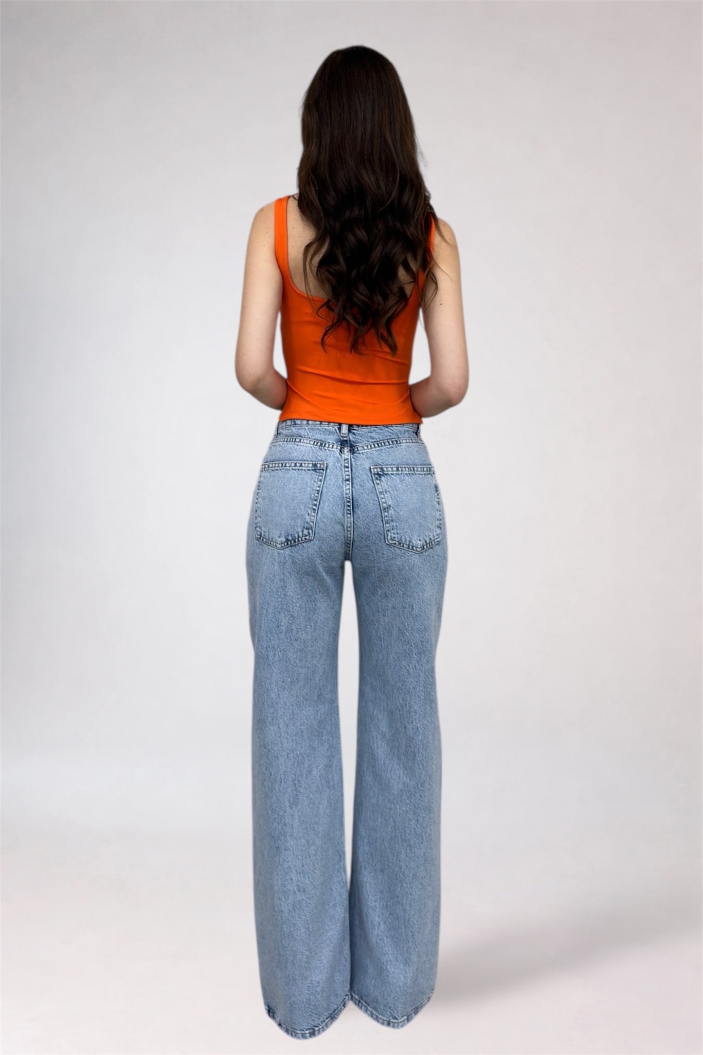 Person wearing an orange tank top and light blue jeans on a white background