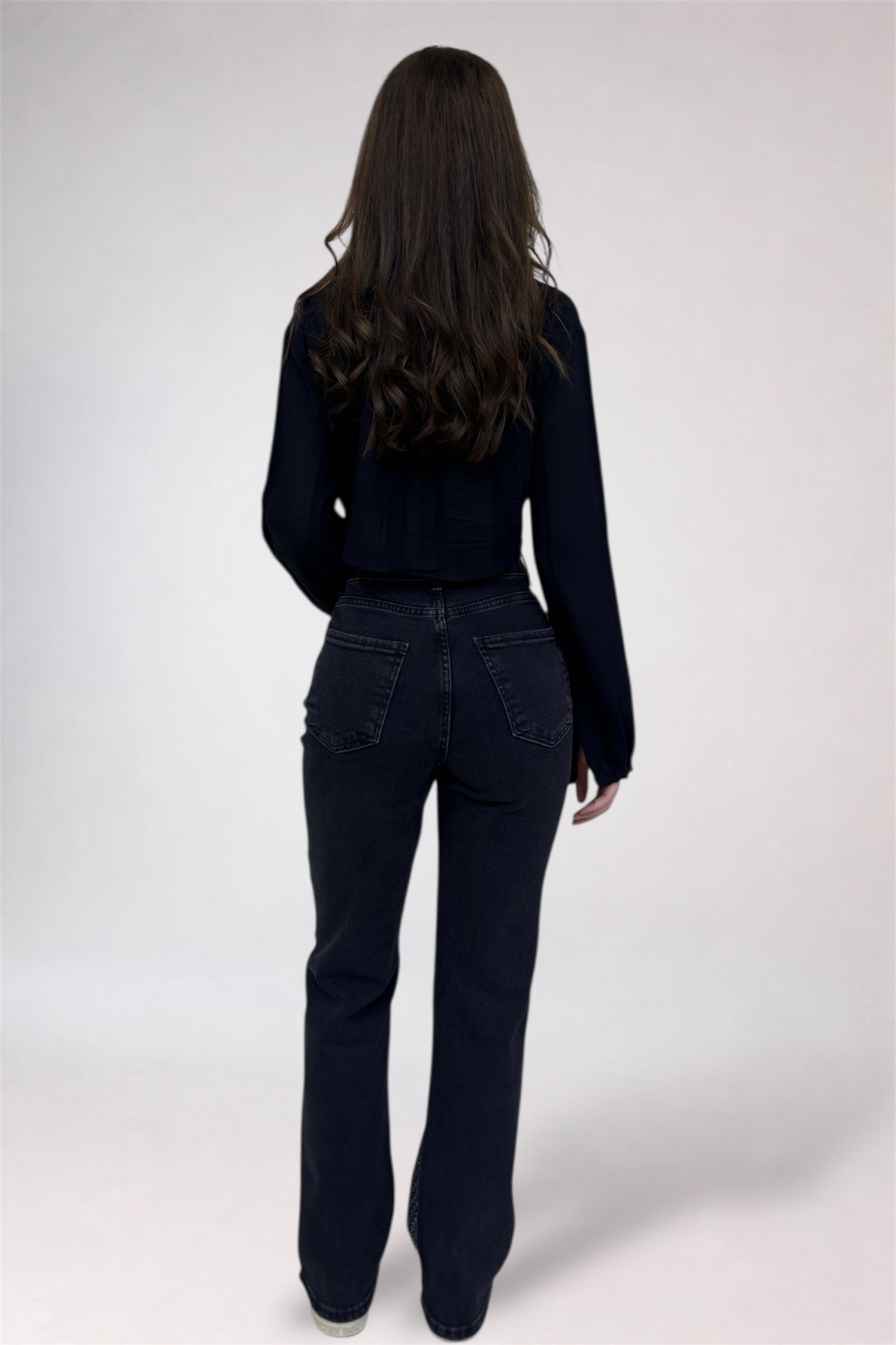 Person wearing a black outfit with flared jeans on a white background