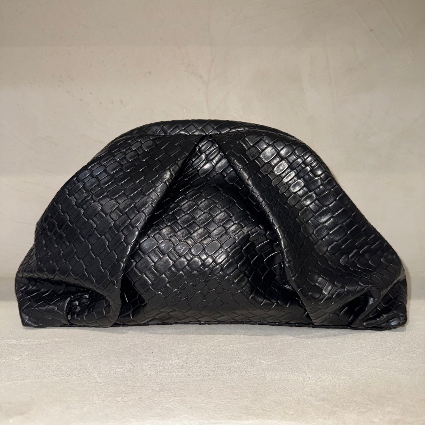 Black textured clutch bag on a light beige background