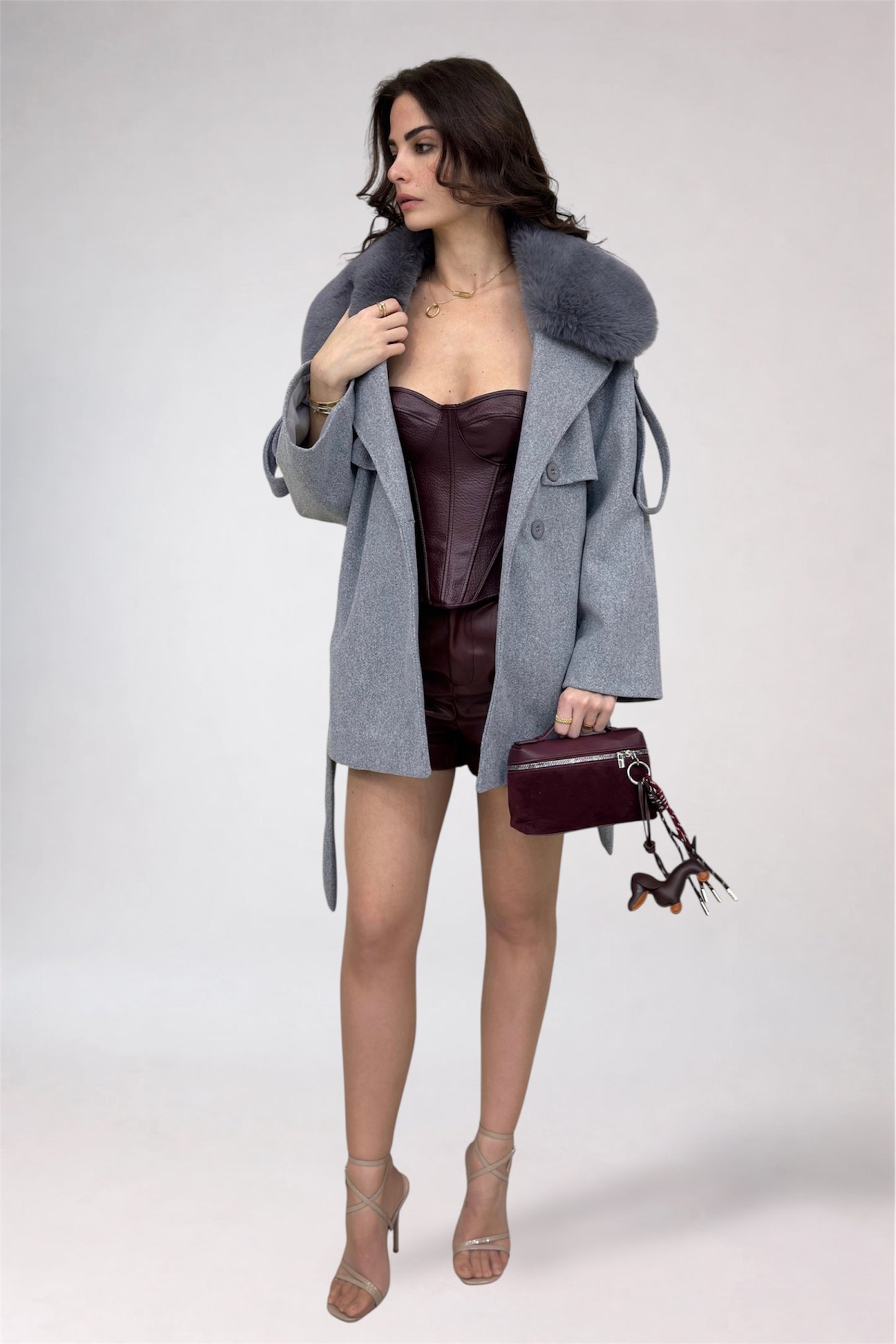 Woman wearing a gray coat with fur hood, dark dress, and holding a matching handbag on a white background