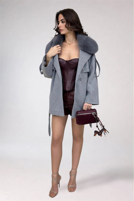 Woman wearing a gray coat with fur hood, dark dress, and holding a matching handbag on a white background