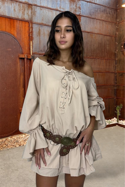 Woman wearing a beige off-shoulder dress with lace details in a rustic setting.