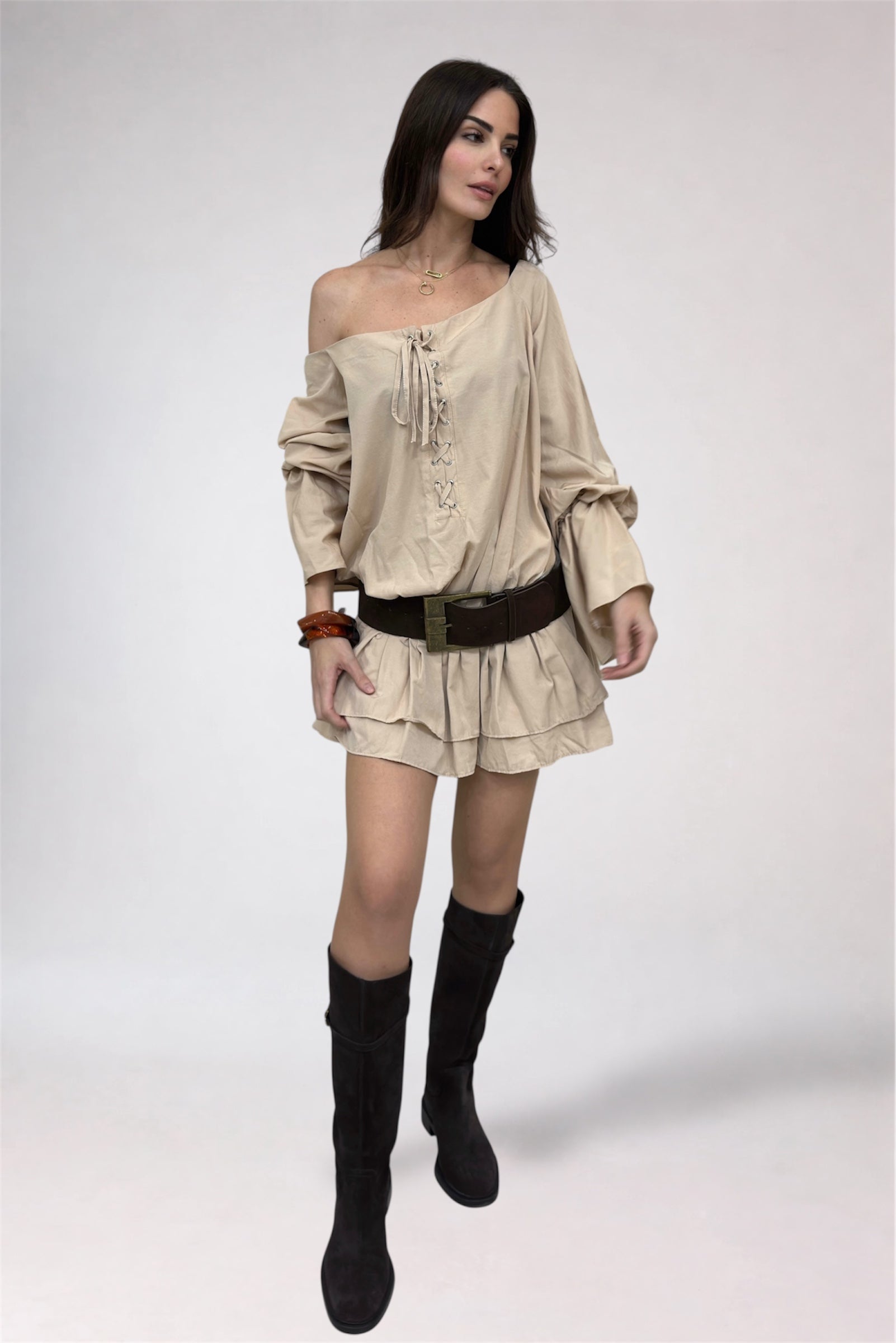 Woman wearing a beige off-shoulder top and skirt with black knee-high boots on a white background
