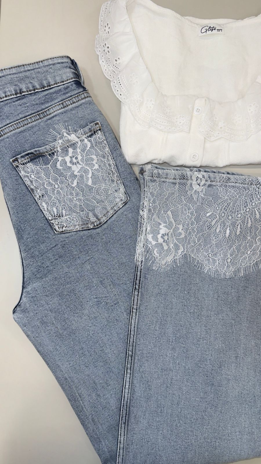 White lace top and blue jeans with lace detailing on a neutral background