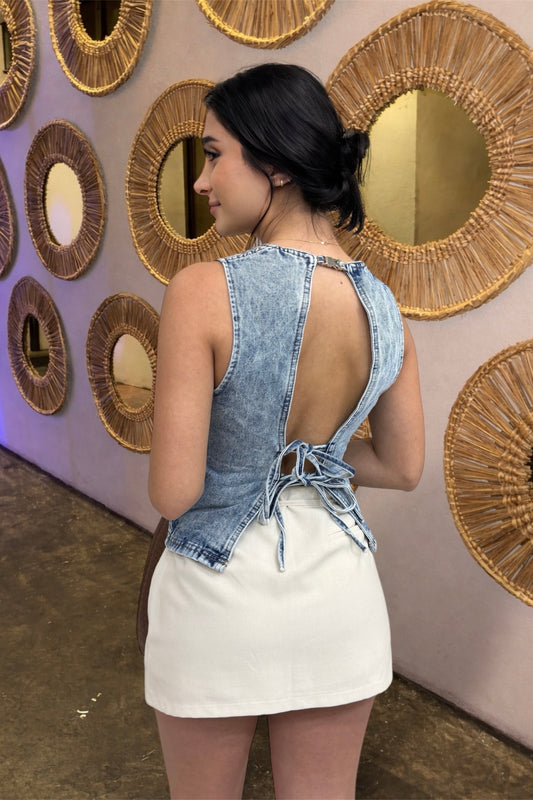 Woman wearing a denim top with a cut-out back design in front of decorative wall mirrors.