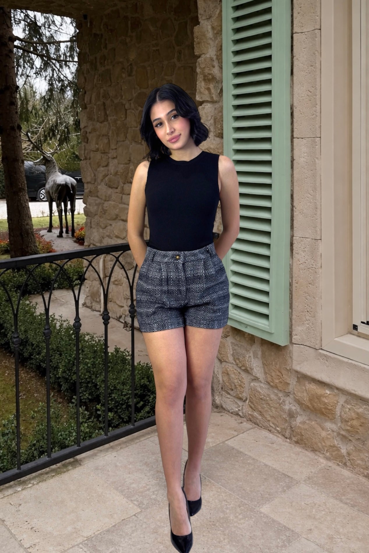 Woman in black sleeveless top and gray shorts standing on a stone porch.
