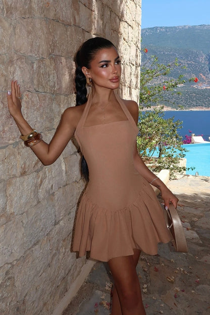 Woman in a beige dress standing against a stone wall with a scenic background