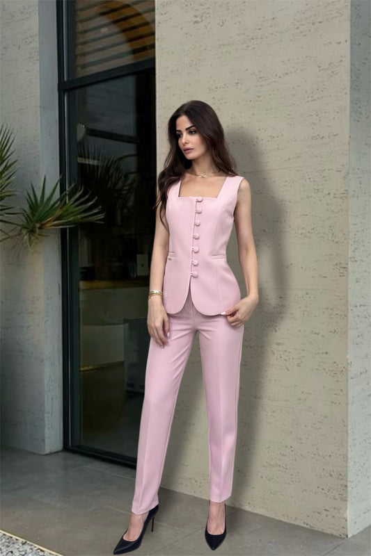 Woman in a pink suit standing against a neutral wall.