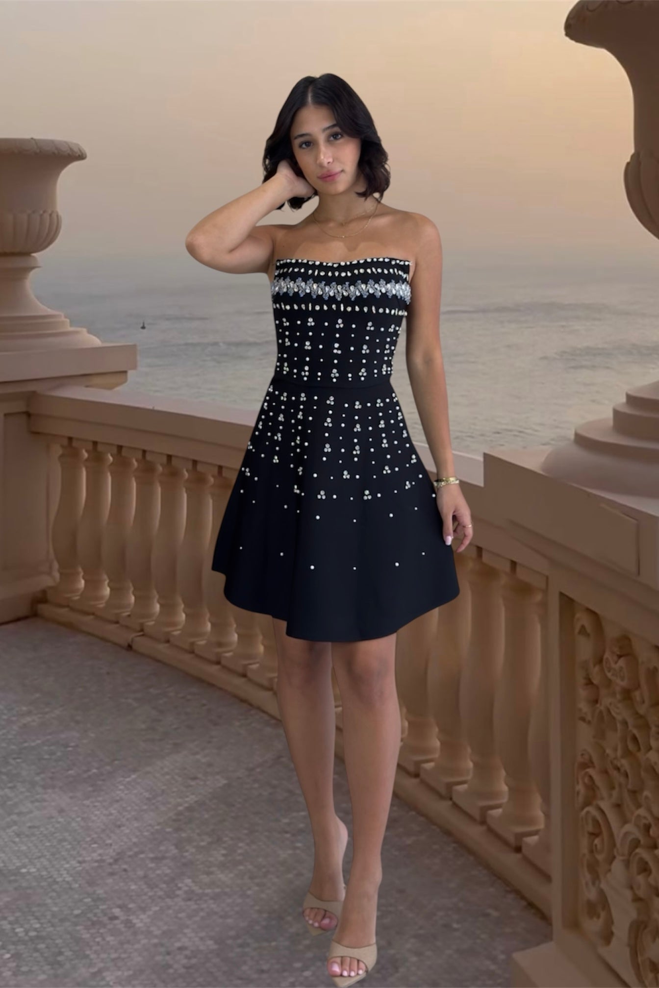 Woman in a strapless black and white dress standing on a balcony with a scenic background.