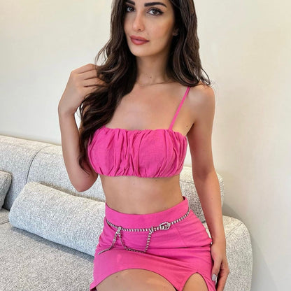 Woman wearing a bright pink outfit with a top and skirt, sitting on a couch.